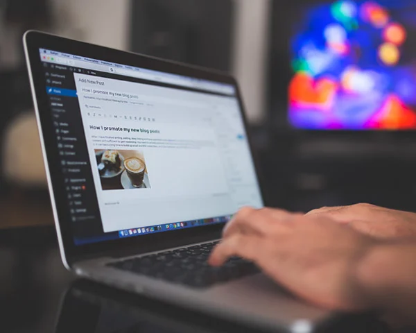 Hand typing on a laptop showing the WordPress Add New Post editor, illustrating a content management system for hotels