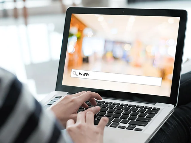 Hands typing on a laptop with a www. search bar on screen, illustrating campaigns that send guests to a hotel website