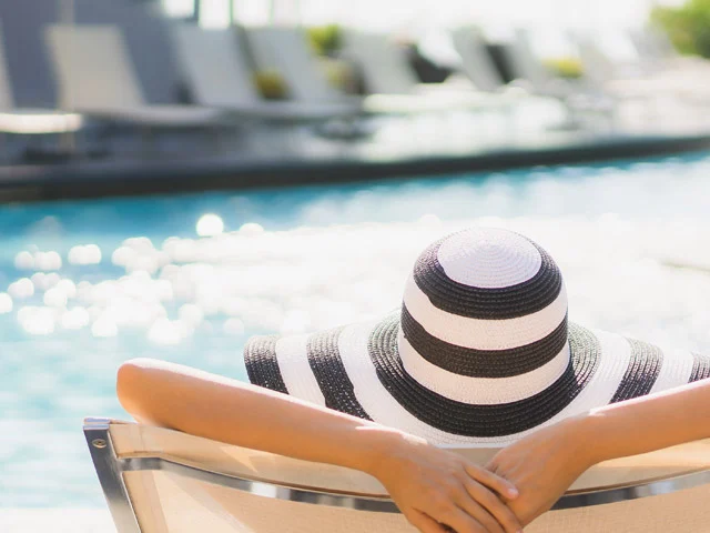 Woman in a striped black and white sun hat lounging by a sparkling hotel pool, representing rooms sold via a channel manager