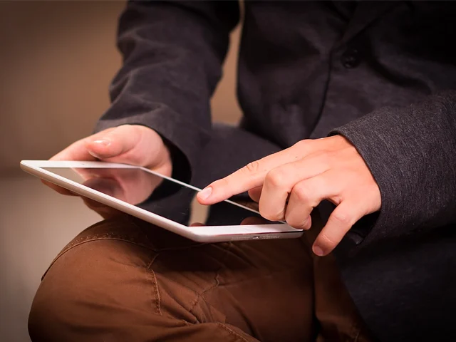 Hands tapping a white tablet resting on a knee, showing travelers booking a stay directly with a hotel