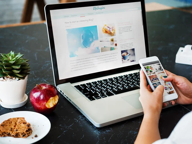 Laptop showing a blog site and a hand holding a phone with its mobile view, illustrating hotel website design for conversions
