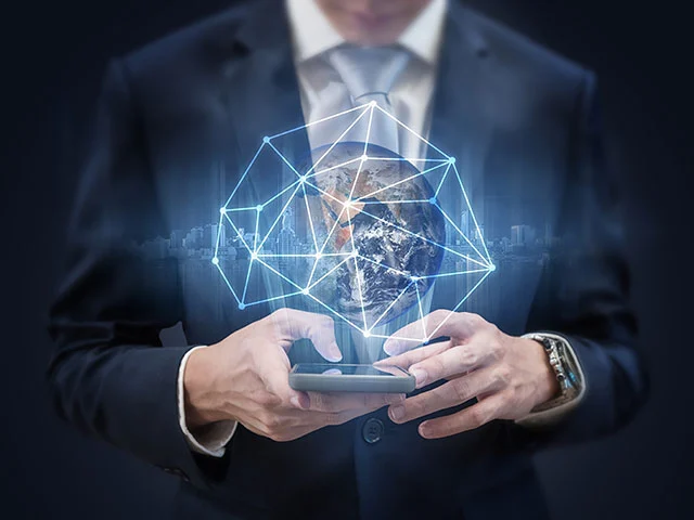 Businessman holding a smartphone under a glowing globe and network hologram, representing hotel technology providers