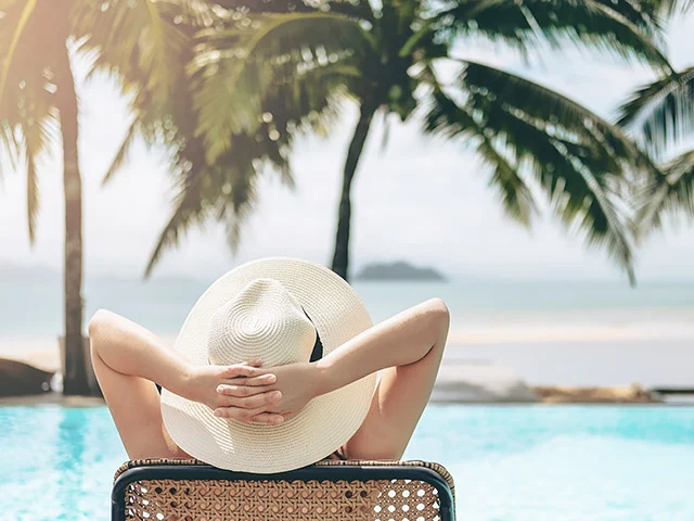 Woman in a straw sun hat relaxing on a lounger by a pool with palm trees and sea, imagery that makes a hotel site stand out