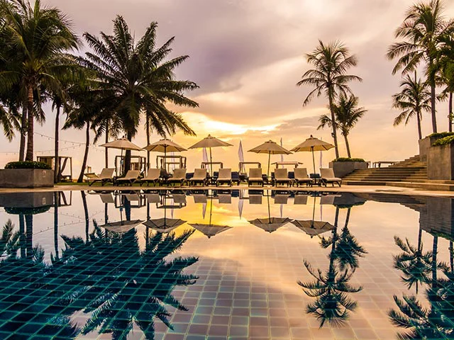 Resort infinity pool at sunset reflecting palm trees, parasols and rows of sun loungers
