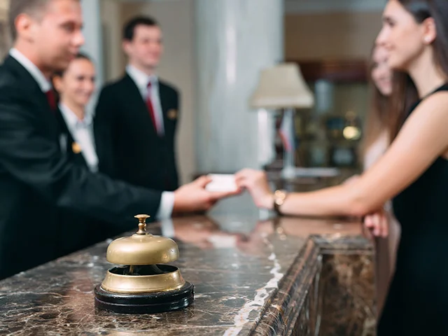 Hotel receptionist handing a key card to a smiling guest across a marble desk with a service bell