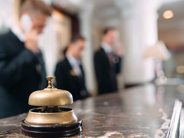 Brass service bell on a marble reception desk with hotel staff on the phone blurred behind
