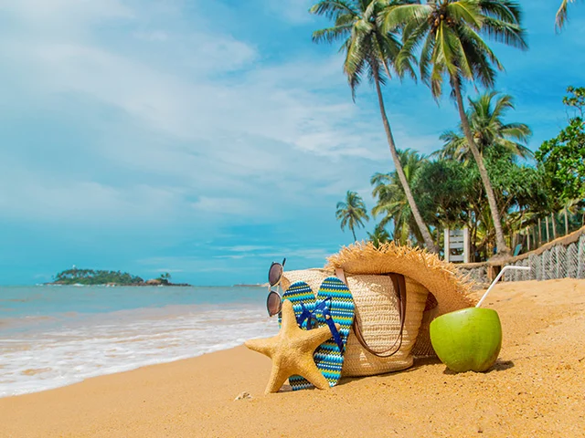 Straw hat, bag, flip-flops, starfish and coconut on a tropical beach with palm trees, evoking summer travel